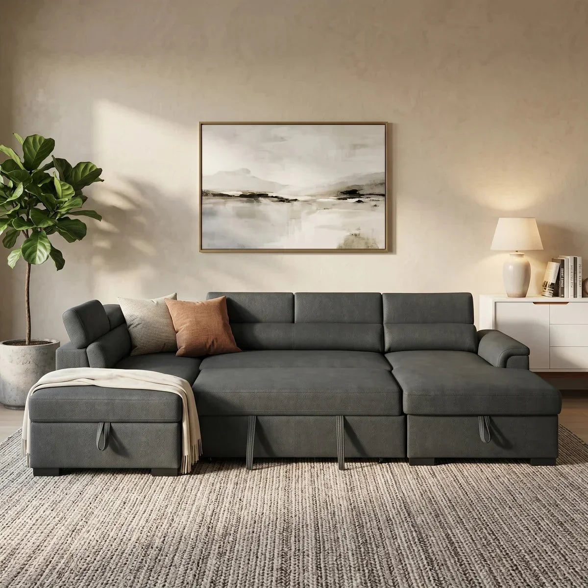 Contemporary living room featuring a dark gray Omaha Pull-Out Sofa Bed with plush cushions, a chaise lounge, and neutral-toned decor including a houseplant, abstract wall art, and a table lamp.