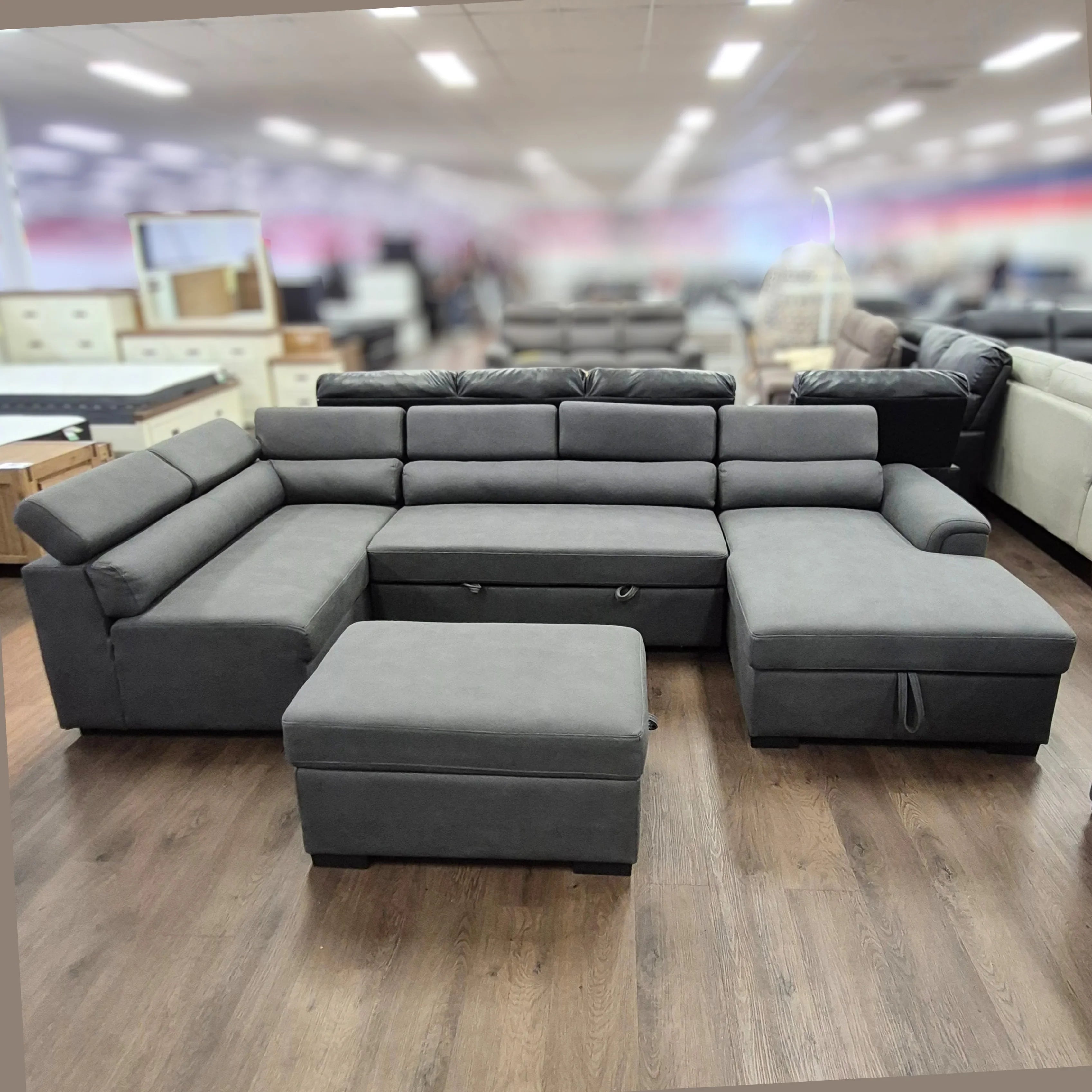 Grey pull-out sofa bed with ottoman on wooden floor in furniture showroom