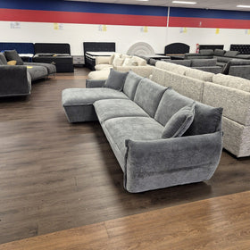 Opal L-shaped fabric lounge with chaise in dark grey, angled view showing the deep seats, curved arms and scatter cushions, in The A2Z Furniture showroom