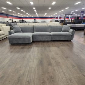Opal L-shaped fabric lounge with chaise in dark grey, photographed front-on with the chaise on the right when sitting, on the floor of The A2Z Furniture showroom