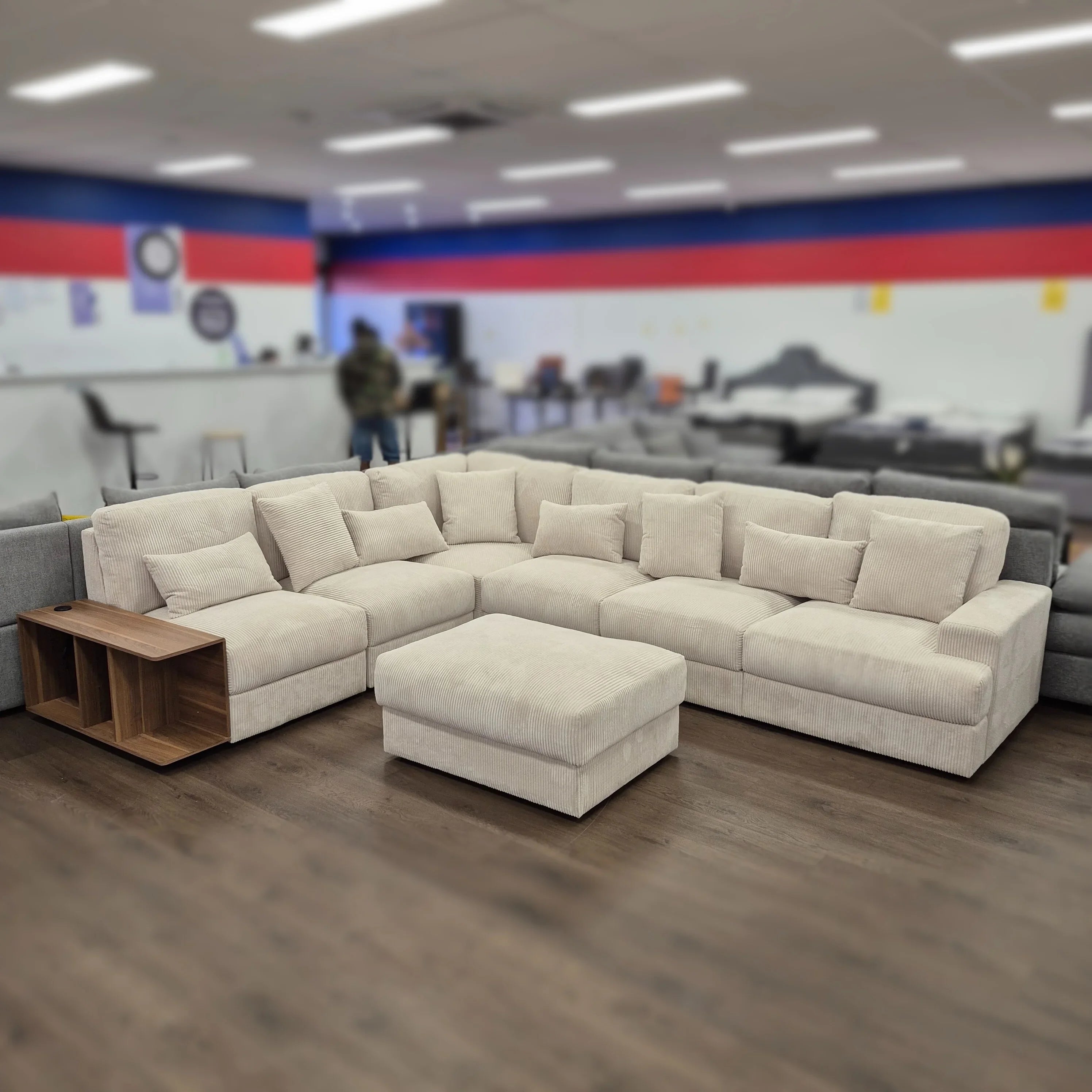 Large beige corduroy sectional sofa with ottoman and wooden side table in furniture showroom