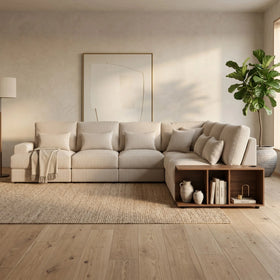 Opulence Corner Sofa in a light beige fabric with a modern design, featuring plush cushions, a built-in wooden side shelf, and styled in a cozy, minimalist living room.