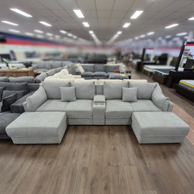 Modern light grey 4 seater sofa with ottoman and cup holders displayed in showroom