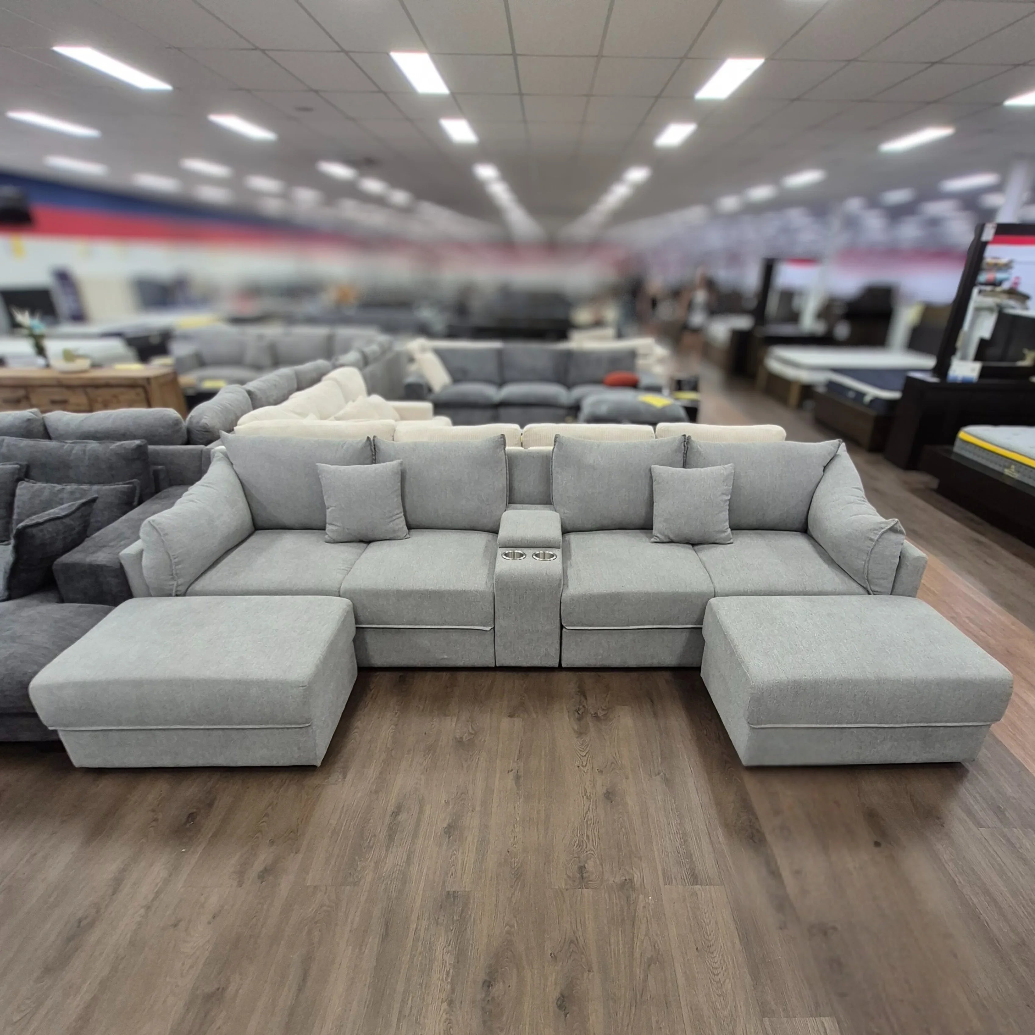 Modern light grey 4 seater sofa with ottoman and cup holders displayed in showroom