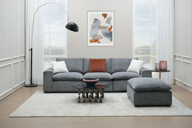 Modern grey sectional sofa set with ottoman in bright living room, glass coffee table, floor lamp, and abstract wall art