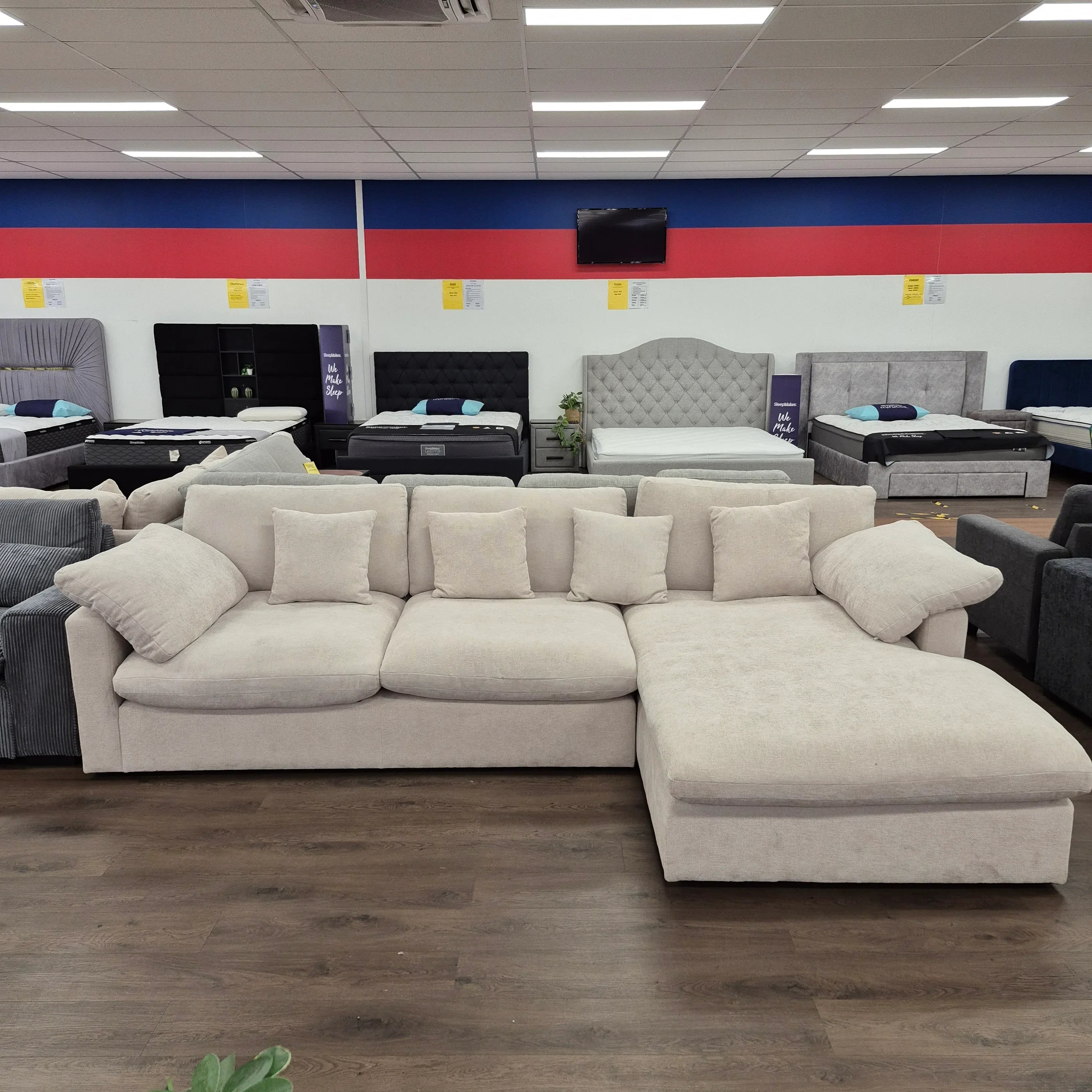 Modern beige sectional sofa with chaise and cushions in a furniture showroom, wooden flooring