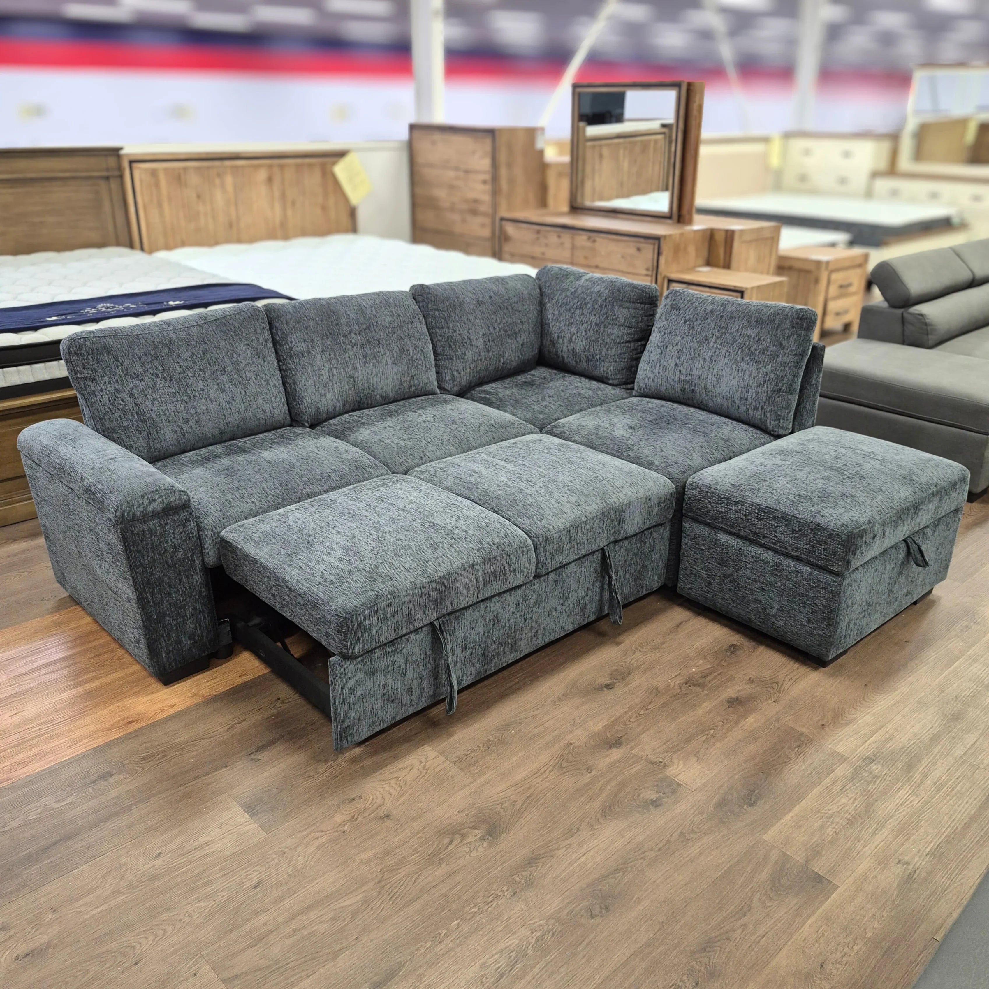 Gray fabric sofa bed with pull-out chaise in furniture showroom on wood flooring