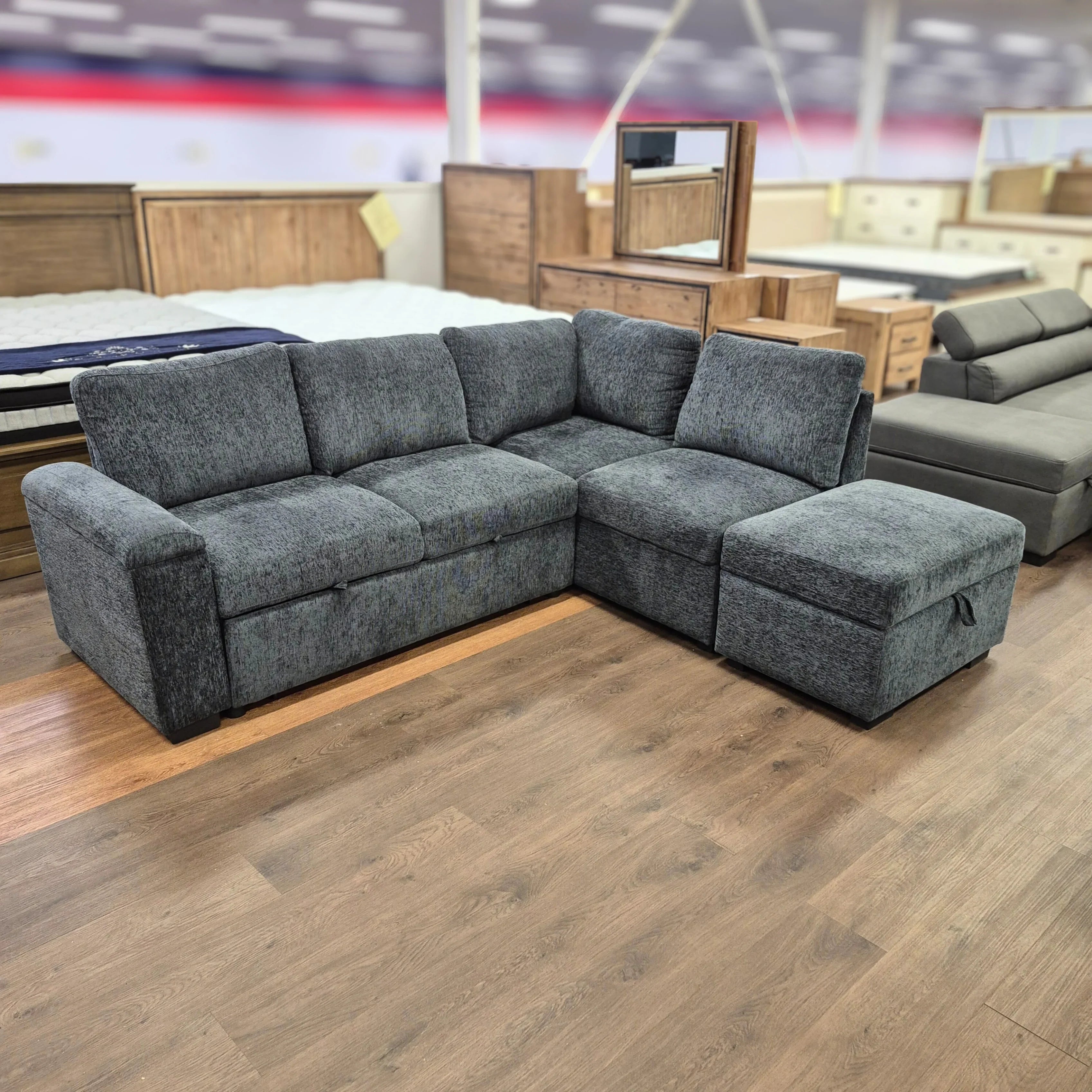 Grey fabric sofa bed with chaise lounge in a furniture showroom, wood floor background