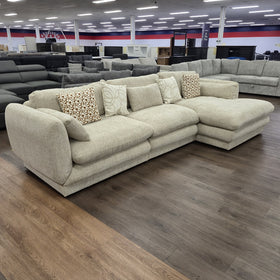 Otway L-Shaped Fabric Lounge in Beige viewed at an angle in the showroom, showing the curved arm profile and deep seat cushions.