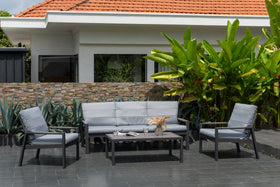 Modern outdoor grey sofa set with coffee table and armchairs on patio, lush garden backdrop