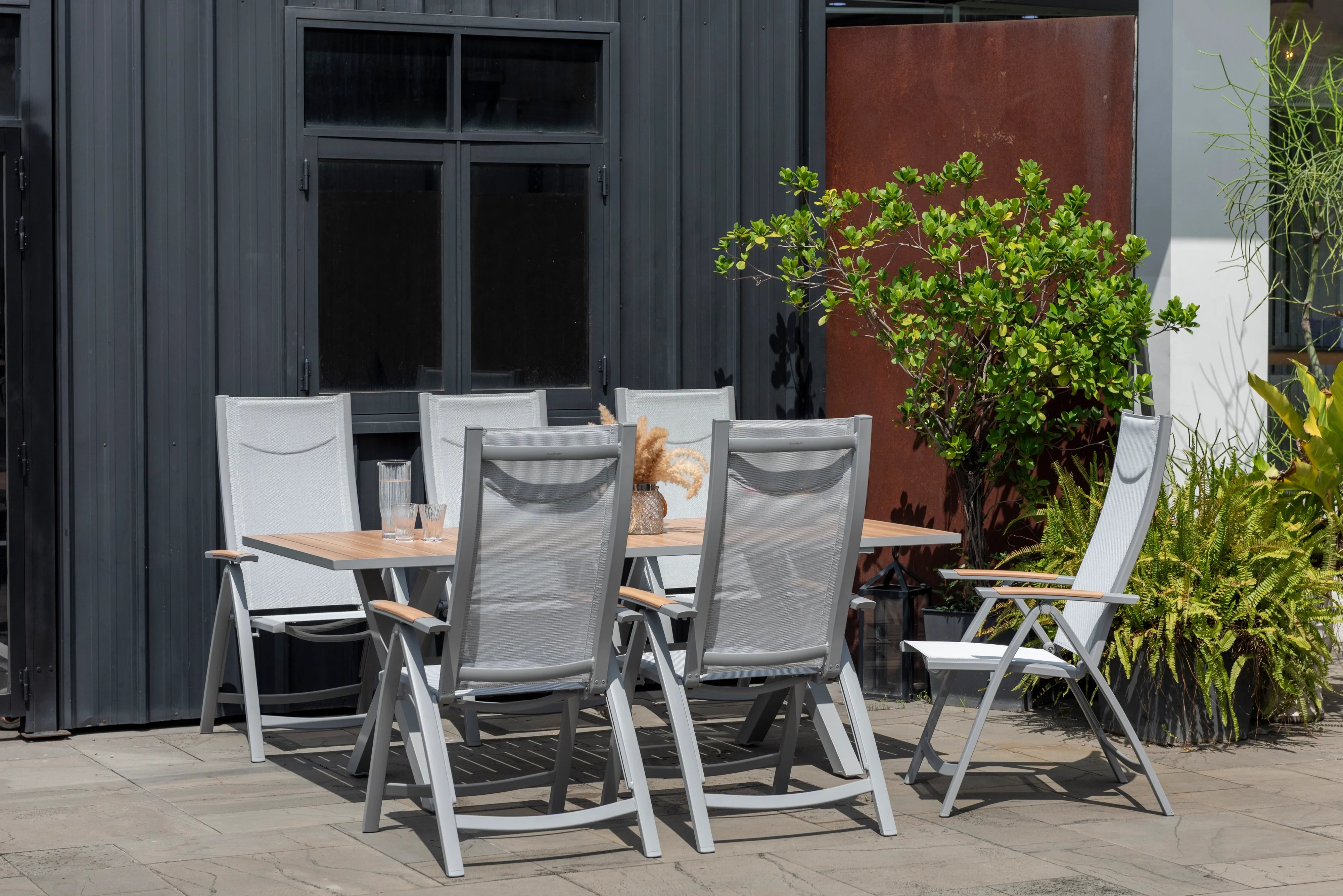 Modern outdoor dining set with six grey mesh chairs and a rectangular timber table on a patio