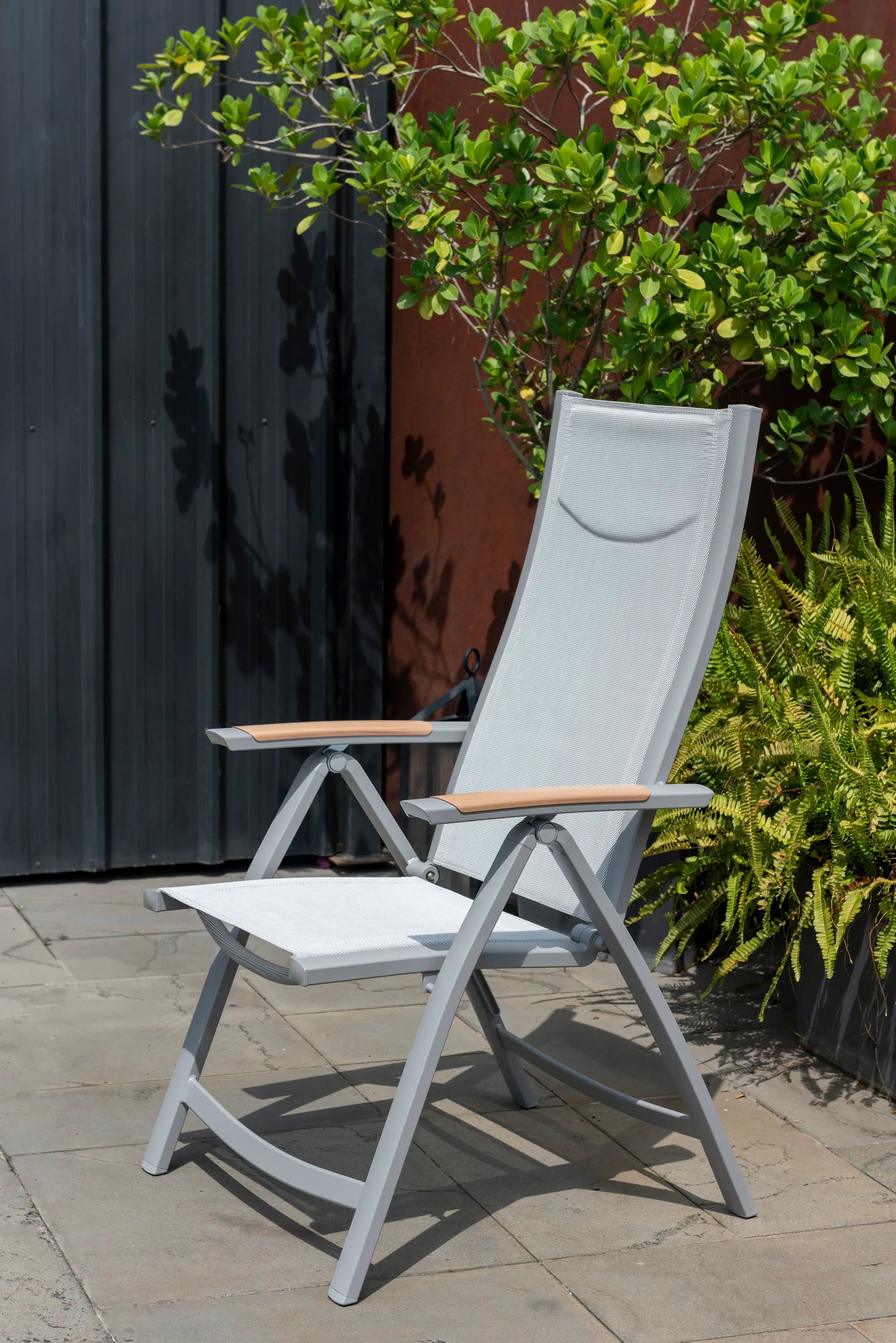 Modern grey outdoor reclining chair with mesh seat and wooden armrests on patio