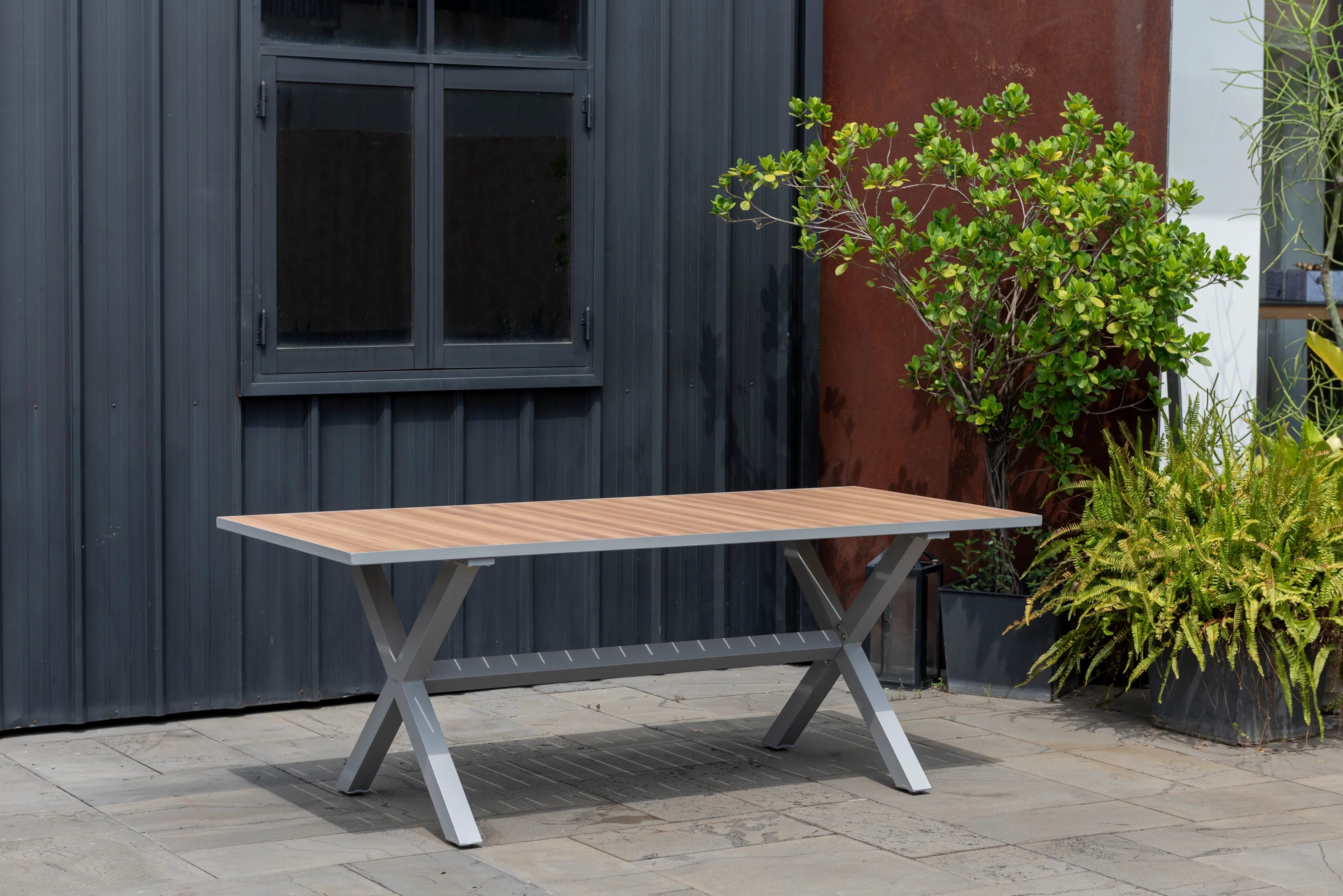 Rectangular outdoor dining table with wood-look top and grey cross legs on patio