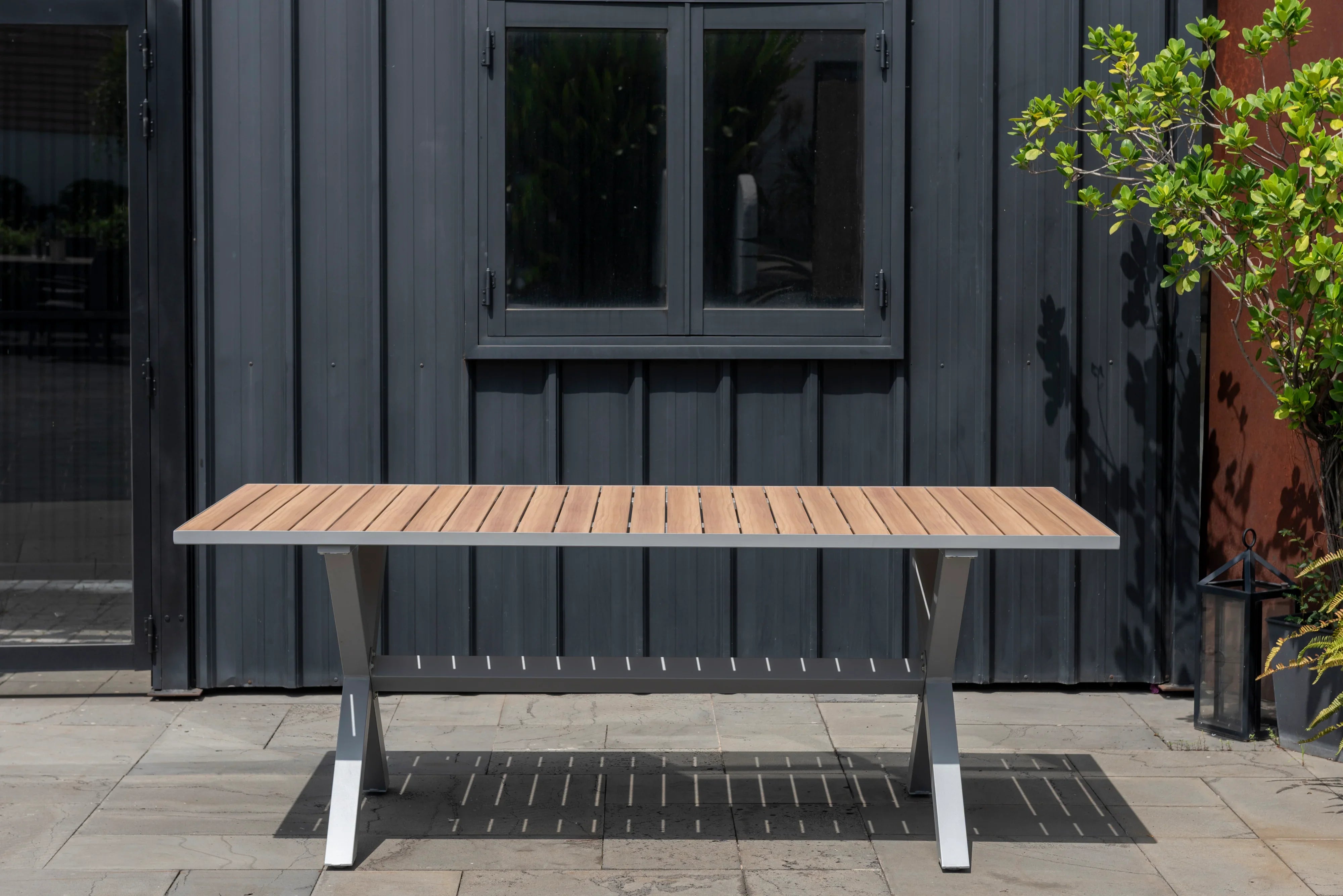 Outdoor rectangular dining table with wood slat top and grey aluminum cross legs on patio