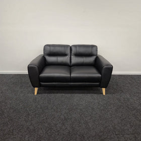 Pearl 2 Seater Leather Lounge in black leather, front view showing two seat cushions, two-section sculpted back and pale timber tapered legs, on display in The A2Z Furniture showroom