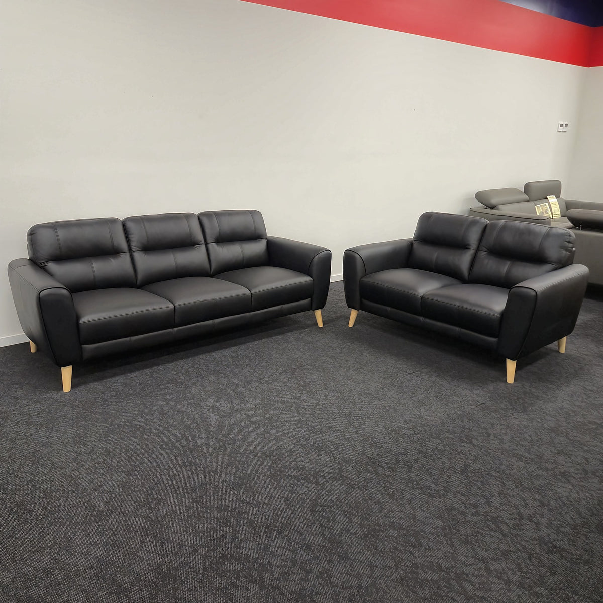 Pearl 3 Seater and 2 Seater Black Sofa Set on display in The A2Z Furniture showroom, the three-seater and two-seater facing each other, both in black leather on pale tapered timber legs