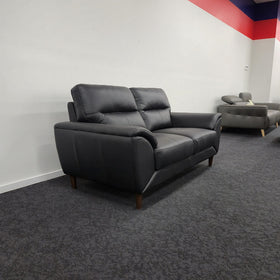 Penrith 2 Seater Leather Sofa in black at a three-quarter angle in The A2Z Furniture showroom, showing the sloped padded armrest and side profile