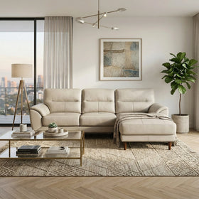 Penrith 3 Seater Leather Sofa with Chaise in beige leather set in a modern living room with glass coffee table, floor lamp, abstract wall art, and potted plant.