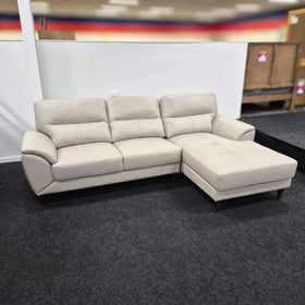 Contemporary beige leather 3 seater sofa with chaise on dark carpet in showroom setting