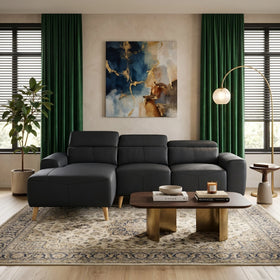 A modern living room featuring the Percy 3 Seater Leather Lounge with Chaise in black, paired with a wooden coffee table, green curtains, abstract wall art, and a stylish floor lamp.