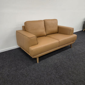 Picasso 2 Seater Leather Lounge in Orange leather, three-quarter view showing the leather grain, stitched cushions and splayed walnut-coloured wooden legs, in The A2Z Furniture showroom.