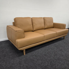 Picasso 3 Seater Leather Lounge in Orange leather, three-quarter view showing the leather grain, stitched seat cushions and broad armrest, in The A2Z Furniture showroom.