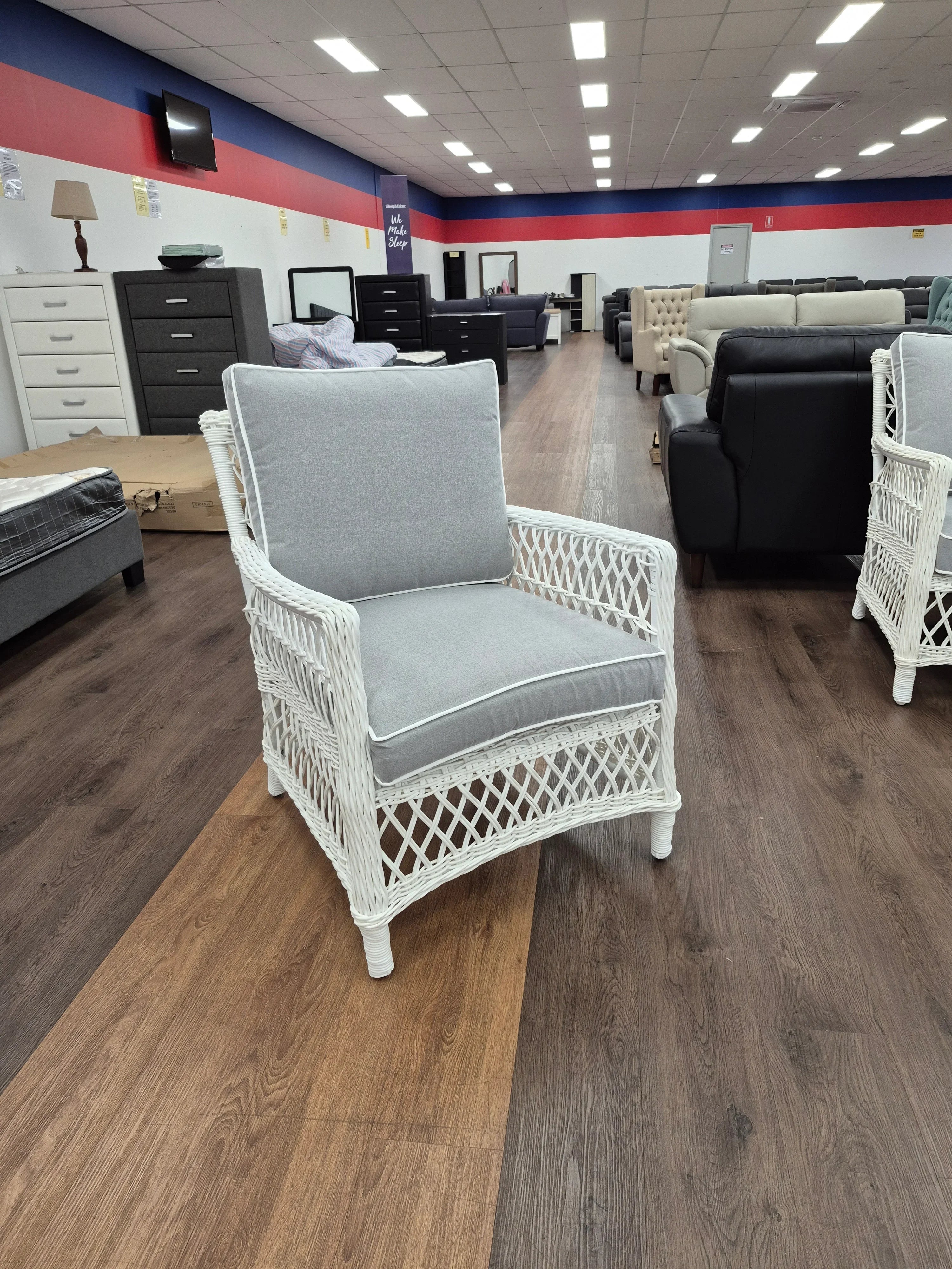 White wicker armchair with grey cushions on display in a furniture showroom