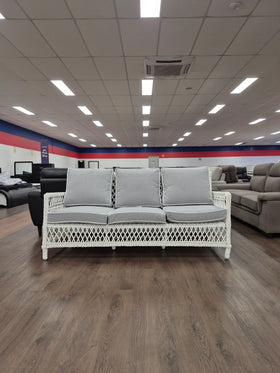 White wicker three-seat sofa with grey cushions in a furniture showroom on wood flooring