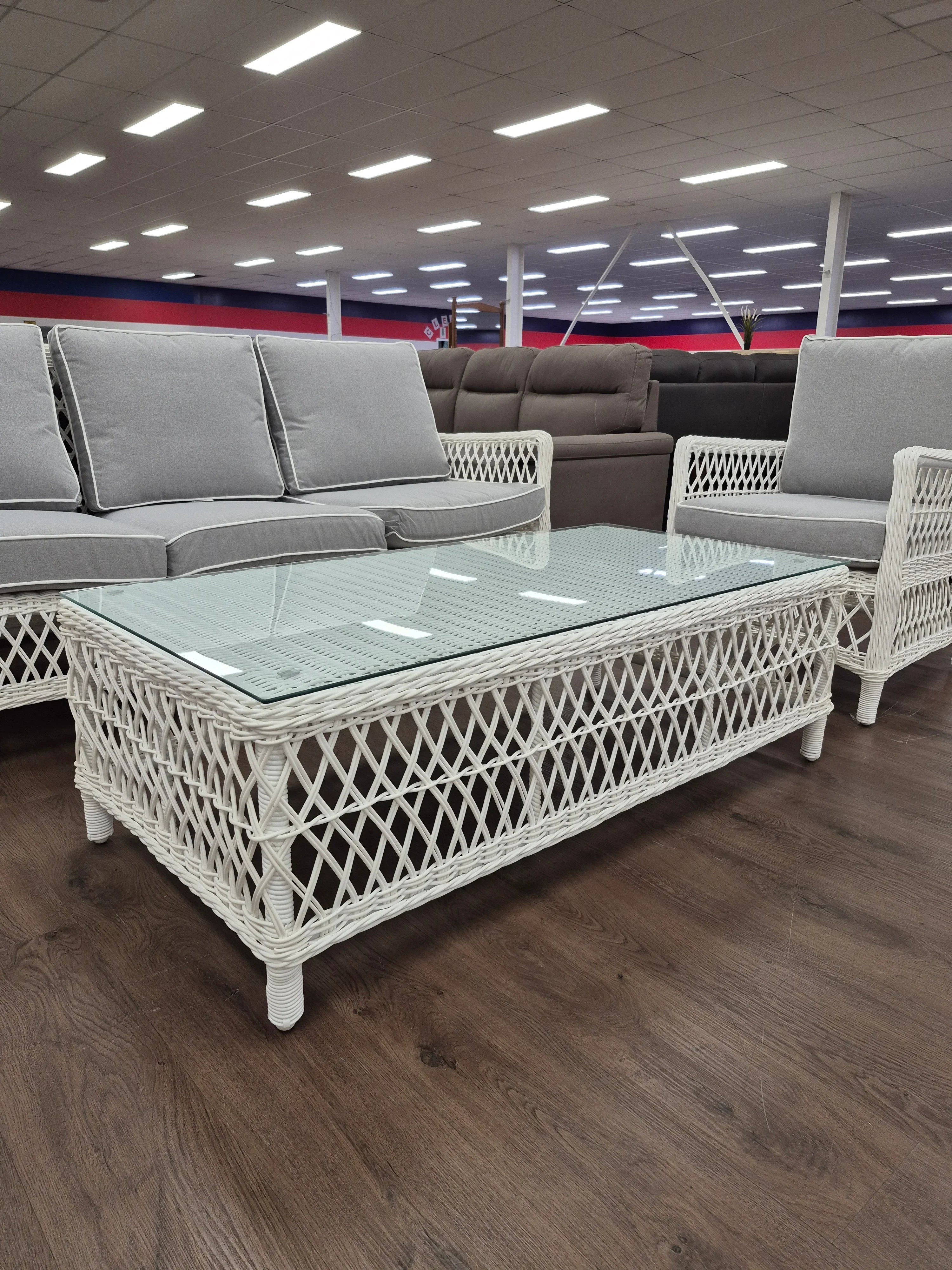 White wicker outdoor lounge set with grey cushions and glass top coffee table in showroom
