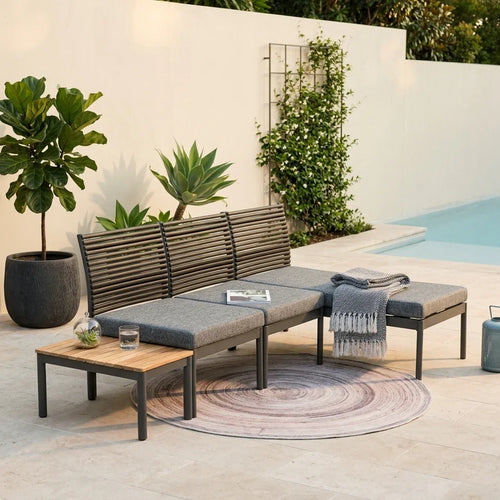 Outdoor patio set with sofa, coffee table, and rug by a poolside.