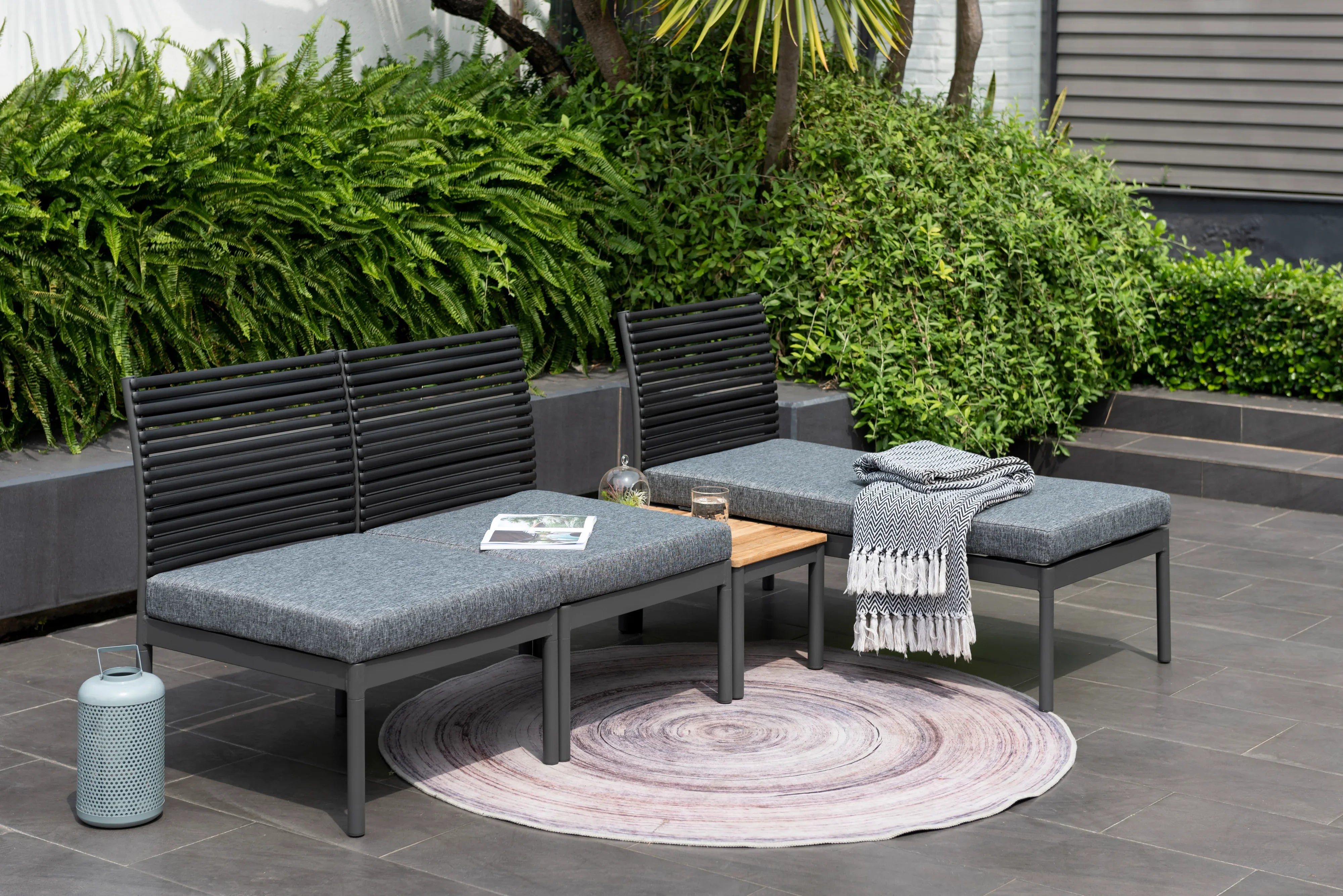 Modern outdoor sofa set with grey cushions, black frames, and side table on a patio