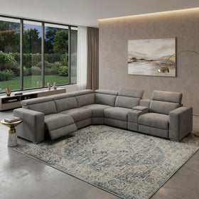 Modern living room featuring a stylish Sandringham Corner Recliner Lounge in grey upholstery with adjustable recliner sections, a decorative rug, and large windows showcasing greenery outside.
