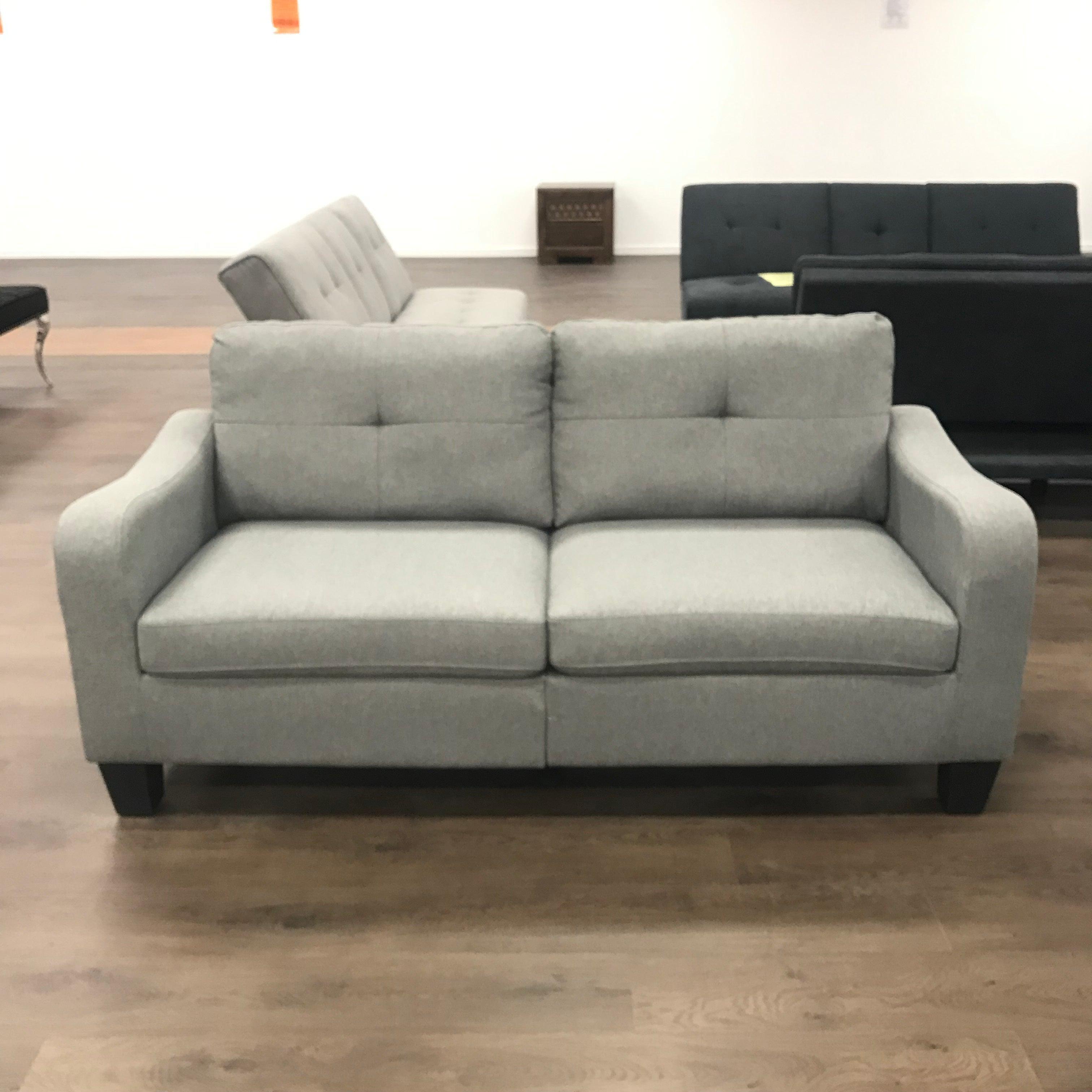 Modern light grey fabric sofa with tufted cushions in a showroom on wood flooring