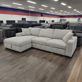 Seaford Corner Sofa Bed in Light Grey viewed at an angle in the showroom, showing the L-shape and the storage chaise closed.