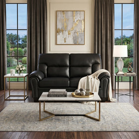 Sebastian 2 Seater PU Leather Sofa in black, styled in a modern living room with a marble top coffee table, decorative accents, and large windows with curtains.