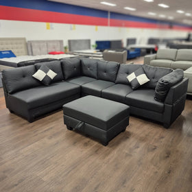 Black PU leather sectional sofa with matching ottoman and accent pillows in showroom