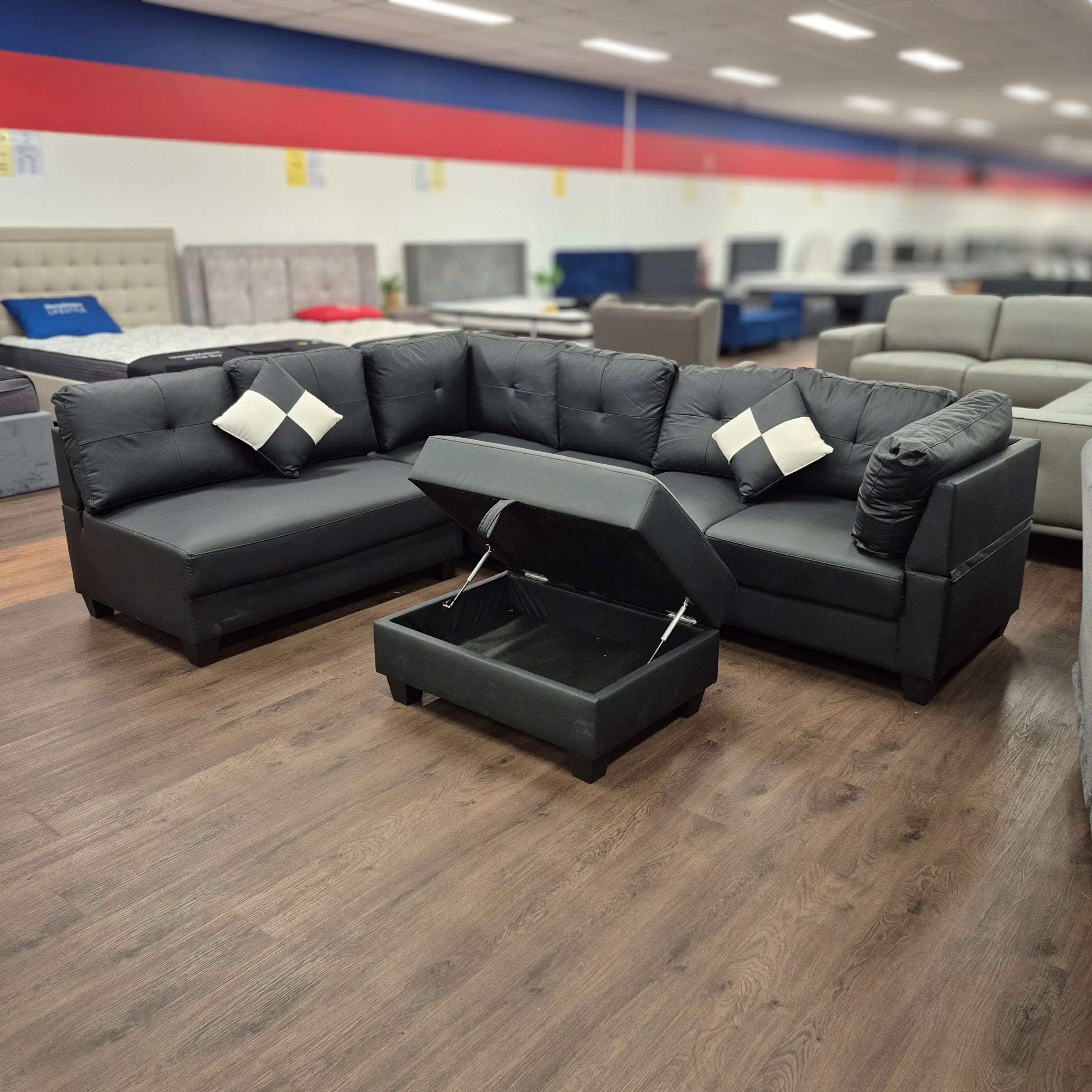 Black PU leather ottoman with open storage, set in a showroom with sectional sofas