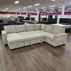 Springbrook Corner Sofa Bed in Grey viewed from the chaise side in the showroom, showing seat depth and the pull-tab for the bed mechanism.