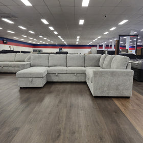 Springbrook Corner Sofa Bed in Grey photographed front-on in the showroom, showing the full width of the seating.