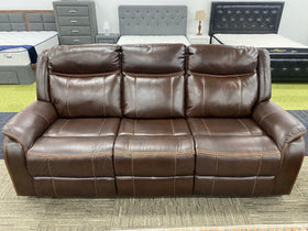 Brown leather recliner sofa in a furniture showroom with beds and bedroom sets in the background