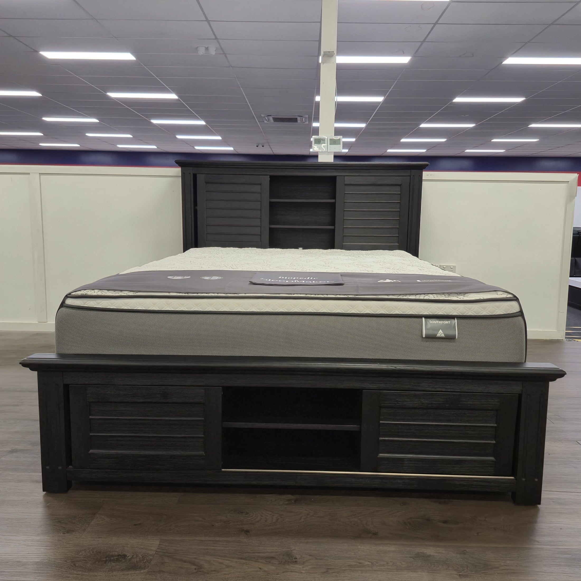 Warwick Bookcase Bed Frame in dark timber finish, full showroom view showing headboard bookcase shelving and footboard storage shelf, at The A2Z Furniture showroom. Mattress shown is not included.